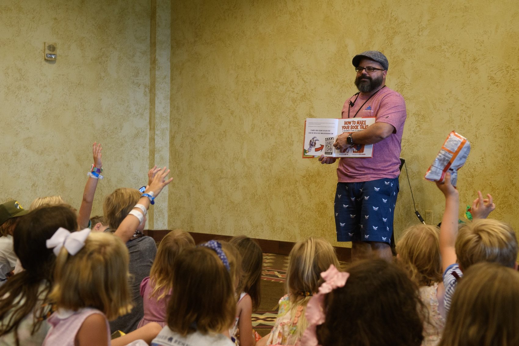 Jimmy Vee reading a picture book to a large group of children with their hands raised